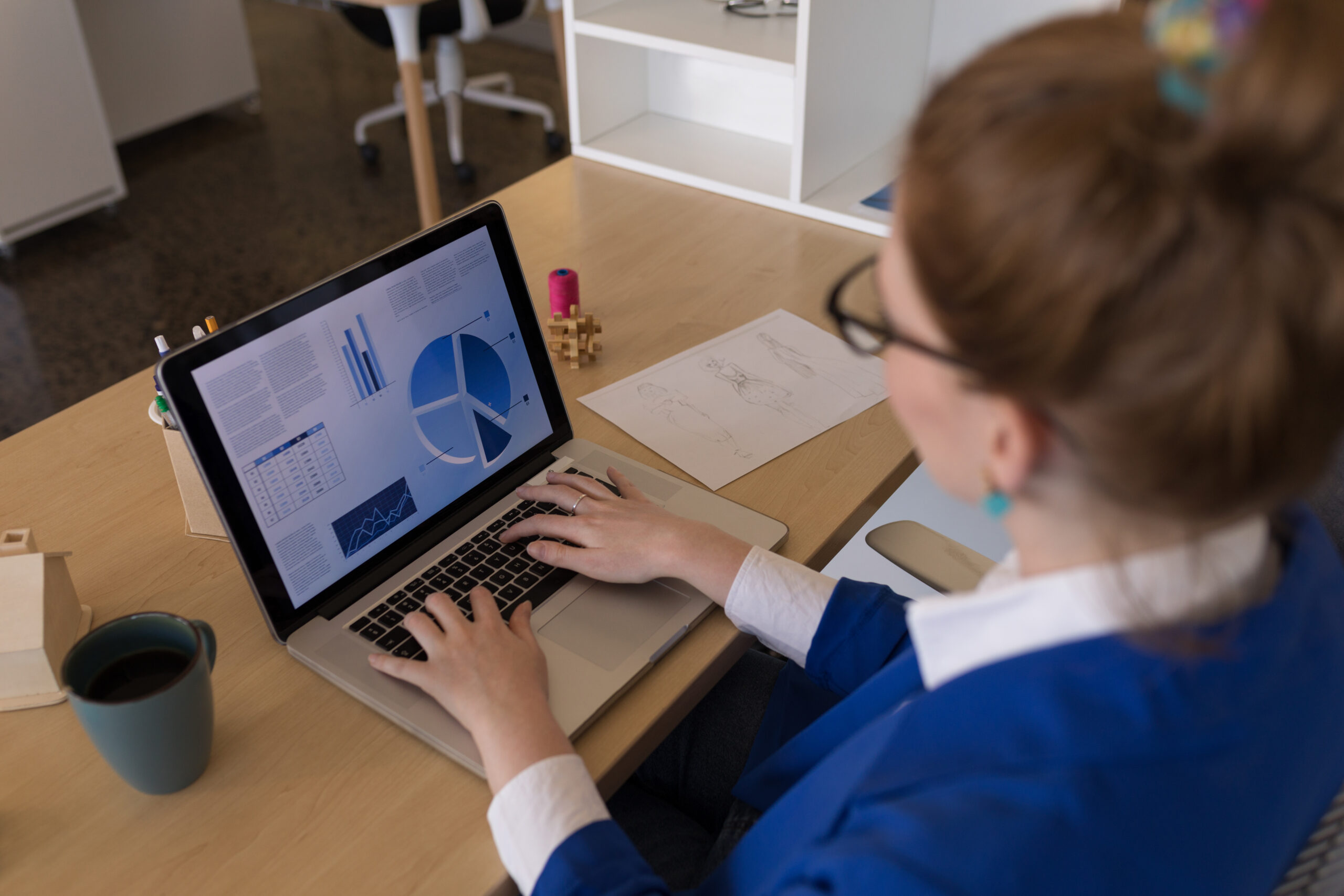 High angle view of pretty Caucasian businesswoman using laptop at desk in modern office